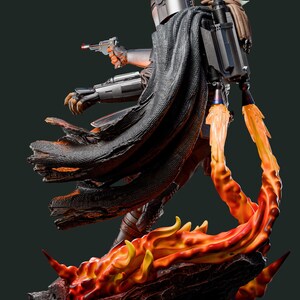 May include: A detailed statue of a character from a science fiction series, clad in silver armour and a black cape, holding a blaster. The figure is mounted on a base with fiery orange and yellow flames, with a small green creature on its back.