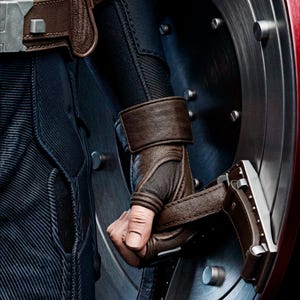 May include: Close-up of a Captain America costume, featuring a brown leather glove and strap, holding a silver and red shield. The costume has a blue and black textured design with a silver buckle.