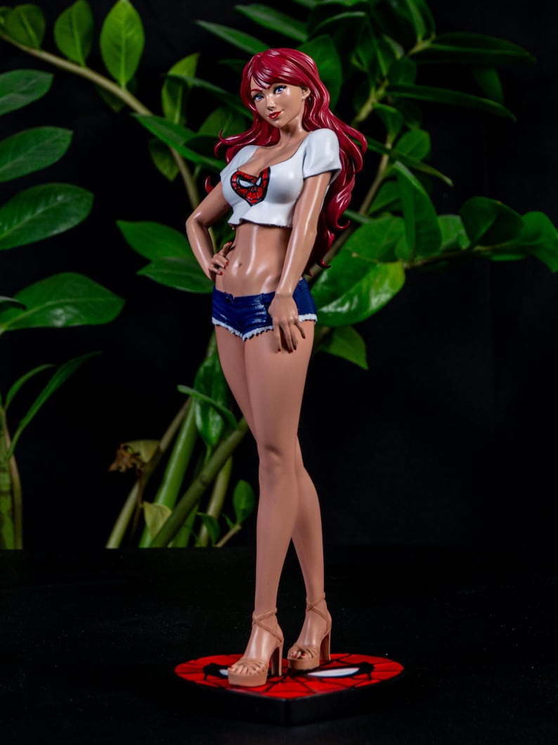 K&ouml;nnte beinhalten: Figur einer Frau mit langen roten Haaren, die ein wei&szlig;es Crop-Top mit Spider-Man-Logo, blaue Jeansshorts und beige High Heels tr&auml;gt. Die Figur steht auf einer rot-schwarzen Basis mit Spinnennetz-Design.