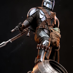 May include: A detailed figurine of The Mandalorian in a dynamic pose, clad in silver and black armor, holding a blaster and a rifle. A small figure of Grogu is in a pouch. The figure is set against a dark, starry background.