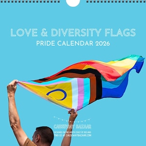 May include: A calendar with the text "LOVE & DIVERSITY FLAGS PRIDE CALENDAR 2026" against a blue background. A person holds up a colorful Pride flag. The flag has various colors and designs, including a yellow section with a blue crescent.