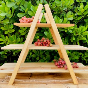 May include: A three-tier wooden shelf in the shape of an A-frame. The shelf is made of natural wood and has three shelves. There are red grapes on each shelf.