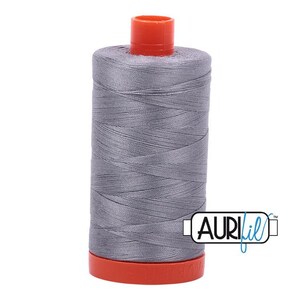 May include: A cylindrical spool of grey sewing thread featuring a bright orange plastic top and base. The spool is wrapped with smooth, fine-textured thread and displays the brand name AURIfil in a black and blue logo on the lower right side.