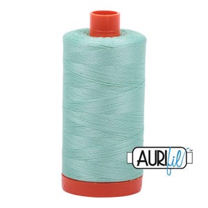 May include: A spool of light mint green sewing thread featuring a bright orange plastic top and base. The spool is cylindrical in shape with the brand name Aurifil printed in black and blue text on a white rectangular label on the side.