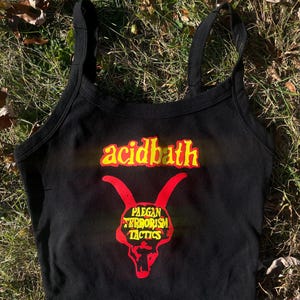May include: Black crop top with spaghetti straps. The top features the text "acidbath" in yellow and a red skull graphic with the text "Paean Terrorism Tactics". The top is made of a soft material.