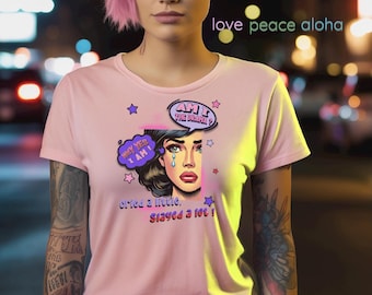 Puede incluir: Camiseta rosa claro con una ilustración de estilo pop art de una mujer llorando. El texto incluye "Why yes I am", "Am I the drama?" y "cried a little, stayed a lot!" con las palabras "love peace aloha".