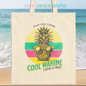 May include: A white canvas tote bag with a retro-style design featuring a pineapple wearing sunglasses and a crown. The text "Wear Your Crown Cool Wahine Strong & Sweet" is printed on the bag.