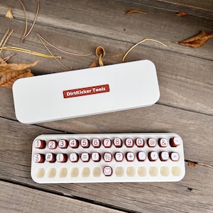 May include: A white and red keyboard-style tool with red number and symbol keys. The tool is open, revealing the keys. The top of the tool has the text "DirtKicker Tools" on a red label.