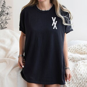 May include: A black oversized t-shirt with a white graphic of two overlapping 'X's on the front.