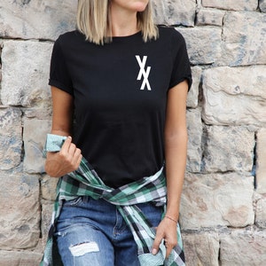 May include: A black t-shirt with a white "XX" graphic on the front. The t-shirt is worn with a green and black plaid shirt tied around the waist.