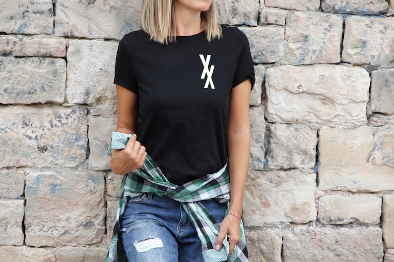 May include: A black t-shirt with a white "XX" graphic on the front. The t-shirt is worn with a green and black plaid shirt tied around the waist.
