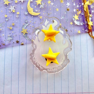 May include: A pair of yellow star-shaped earrings on a clear plastic display card with the word "Sweet" written on it.