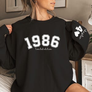 May include: Black sweatshirt with the year "1986" in white block letters, with "limited edition" below. The sleeve features "44 chapter" with a heart. The sweatshirt is a casual style.