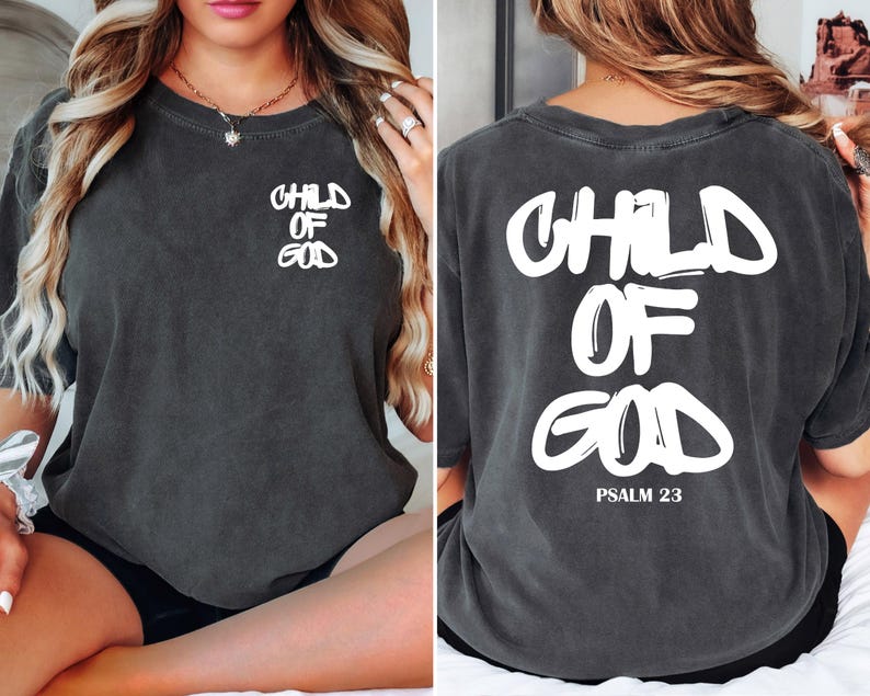 May include: Dark gray t-shirt with the words "CHILD OF GOD" printed in white on the front and back. The back of the shirt also includes "PSALM 23" in white. The shirt has a vintage, worn look.