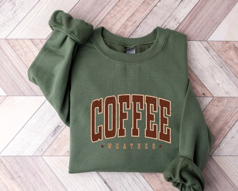 Puede incluir: Una sudadera verde con el texto "COFFEE WEATHER" en letras marrones.