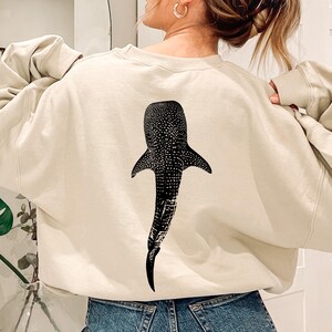 May include: A cream-colored sweatshirt with a black and white whale shark graphic on the back.