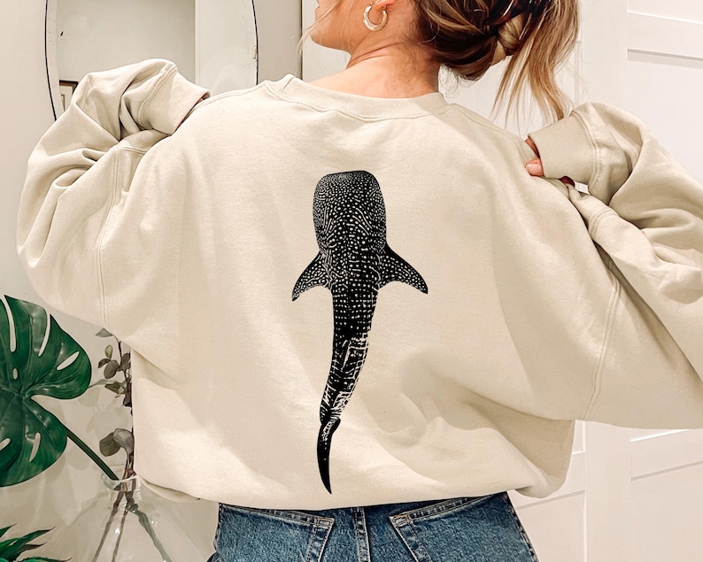 May include: A cream-colored sweatshirt with a black and white whale shark graphic on the back.