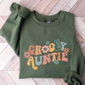May include: Green sweatshirt with a groovy auntie graphic in retro colors with flowers and a peace sign.