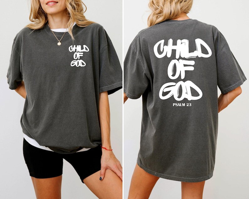 May include: Dark gray t-shirt with white text that reads "CHILD OF GOD" on the front and back. The back of the shirt also includes "PSALM 23" in white text. The shirt has a relaxed fit and short sleeves.