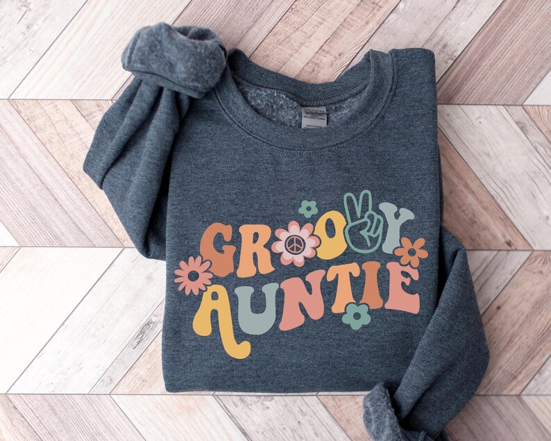 May include: A dark gray sweatshirt with the text "Groovy Auntie" in colorful retro lettering. The text is decorated with peace signs and flowers.