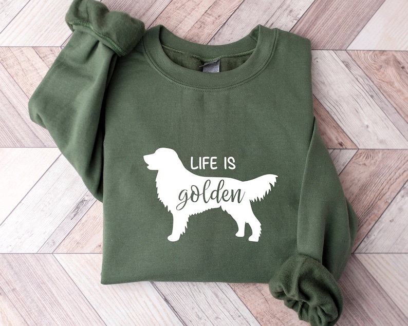 Pu&ograve; includere: Una felpa verde con una silhouette bianca di un golden retriever e il testo "Life is golden".