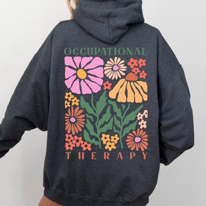 May include: A dark gray hooded sweatshirt with the text "Occupational Therapy" and a colorful floral design on the back.