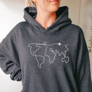 Op de afbeelding: Een donkergrijs hoodie met een witte omtrek van een wereldkaart en een klein vliegtuig dat erboven vliegt.
