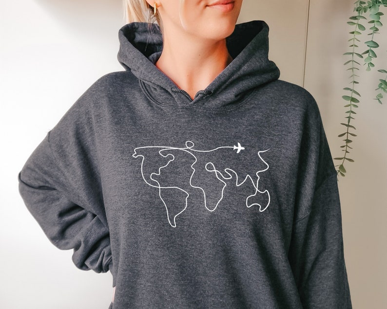 Op de afbeelding: Een donkergrijs hoodie met een witte omtrek van een wereldkaart en een klein vliegtuig dat erboven vliegt.