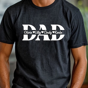 May include: Black t-shirt with white text that reads "DAD" with the names "Olivia", "Lilly", "Cindy", and "Karla" written below in a smaller font.