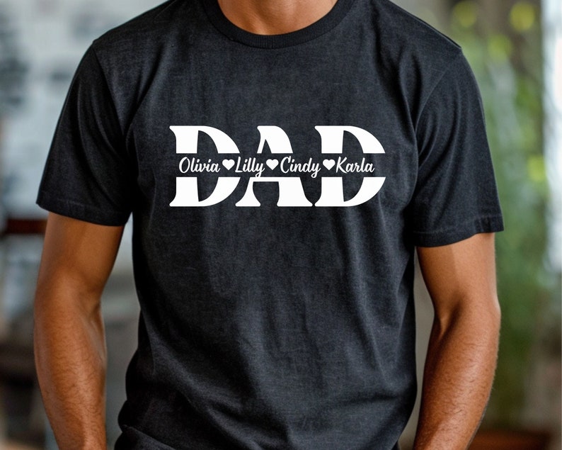 May include: Black t-shirt with white text that reads "DAD" with the names "Olivia", "Lilly", "Cindy", and "Karla" written below in a smaller font.