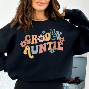 May include: Black sweatshirt with a groovy auntie graphic in retro colors with peace signs and flowers.