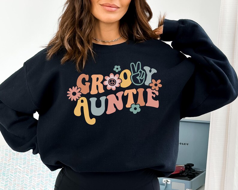 May include: Black sweatshirt with a groovy auntie graphic in retro colors with peace signs and flowers.