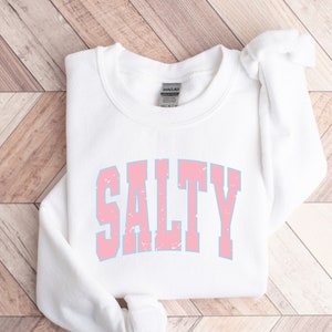 May include: White sweatshirt with a pink and blue "SALTY" graphic printed on the front.