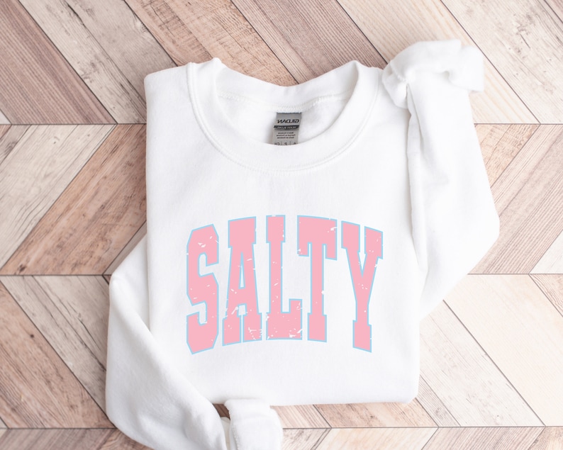 May include: White sweatshirt with a pink and blue "SALTY" graphic printed on the front.
