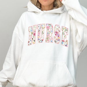 May include: White hoodie with a floral print of the word "NURSE" on the front.
