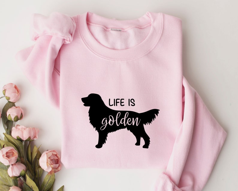 Pu&ograve; includere: Felpa rosa con una silhouette nera di un golden retriever e il testo "Life is golden".