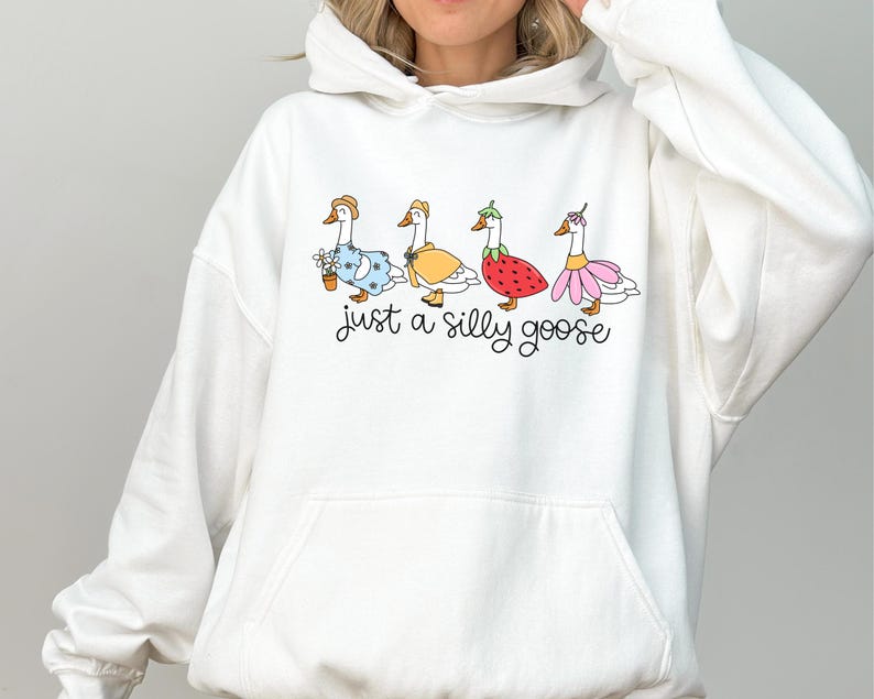 Peut inclure: Sweat-shirt &agrave; capuche blanc avec une illustration fantaisiste de quatre oies v&ecirc;tues de diff&eacute;rentes tenues. Les oies portent une robe bleue, un manteau jaune, un costume de fraise et un tutu rose. Le texte "just a silly goose" est &eacute;crit en dessous.
