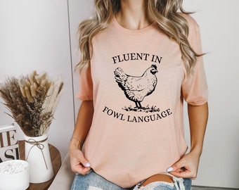 May include: A pink t-shirt with a black graphic of a chicken and the text "Fluent in Fowl Language".