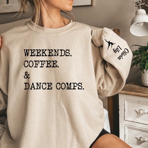 May include: A beige sweatshirt with the text "Weekends. Coffee. & Dance Comps." printed on the front. The left sleeve has a silhouette of a dancer with the text "Olive Branch" printed on the sleeve.