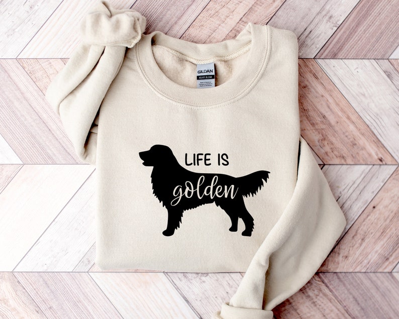 Pu&ograve; includere: Una felpa beige con una silhouette nera di un golden retriever e il testo "Life is golden".