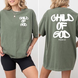 May include: Olive green t-shirt with the text "CHILD OF GOD" in white on the front and back. The back of the shirt also includes "PSALM 23". The shirt is a relaxed fit.