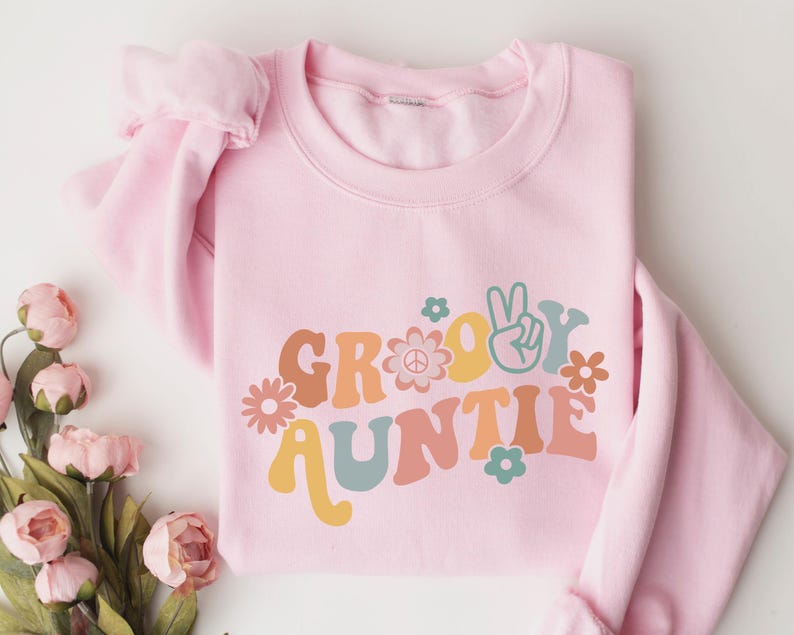 May include: Pink sweatshirt with a groovy auntie graphic in retro colors and a peace sign. The graphic includes flowers and a peace sign.
