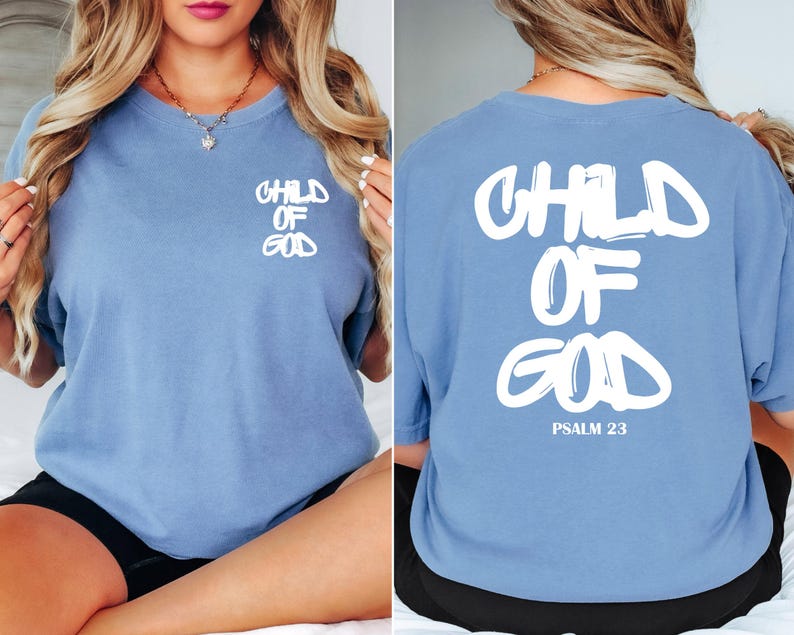 May include: A light blue t-shirt with the words "CHILD OF GOD" printed in white on the front and back. The back of the shirt also includes "PSALM 23" in white. The shirt is a comfortable, casual style.