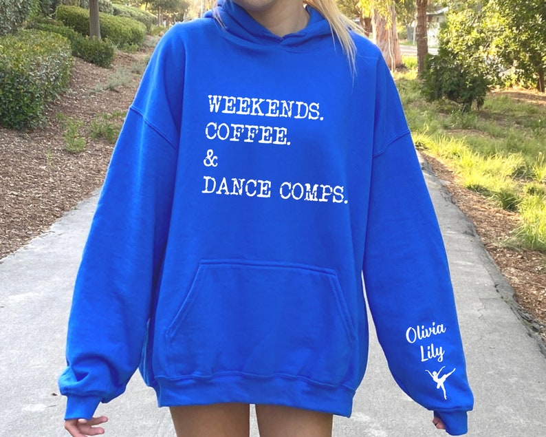 Op de afbeelding: Koninklijk blauwe hoodie met witte tekst die "Weekends. Coffee. & Dance Comps." luidt en een wit danser silhouet op de mouw met de tekst "Olivia Lily".