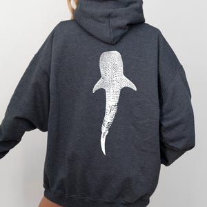 May include: A dark gray hooded sweatshirt with a white whale shark graphic on the back.