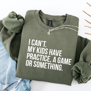 May include: A green sweatshirt with the text "I can't. My kids have practice, a game or something." printed in white.