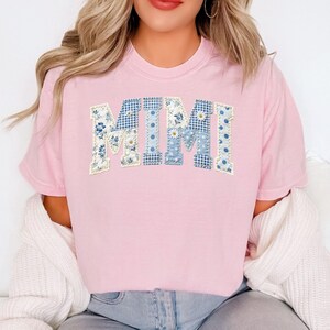 K&ouml;nnte beinhalten: Ein hellrosa T-Shirt mit dem Wort "MIMI" in einem Patchwork-Design. Die Buchstaben bestehen aus blau-wei&szlig;en Blumen- und Tupfenmustern. Das Shirt ist ein l&auml;ssiger Stil.