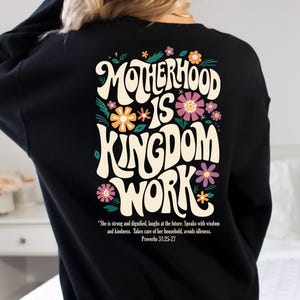 May include: Black sweatshirt with a floral design and the text "Motherhood is Kingdom Work" in a retro font. The text is accompanied by a quote from Proverbs 31:25-27.