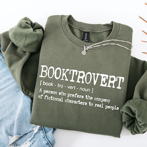 May include: A green sweatshirt with the text "BOOKTROVERT" defined as "[book-tro-vert - noun] A person who prefers the company of fictional characters to real people".