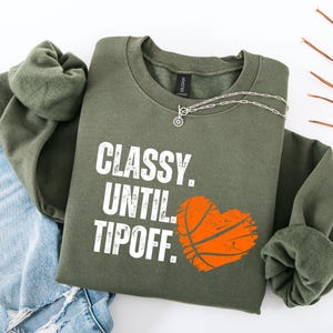 May include: A green sweatshirt with the text "CLASSY. UNTIL TIPOFF." and a basketball graphic in the shape of a heart.